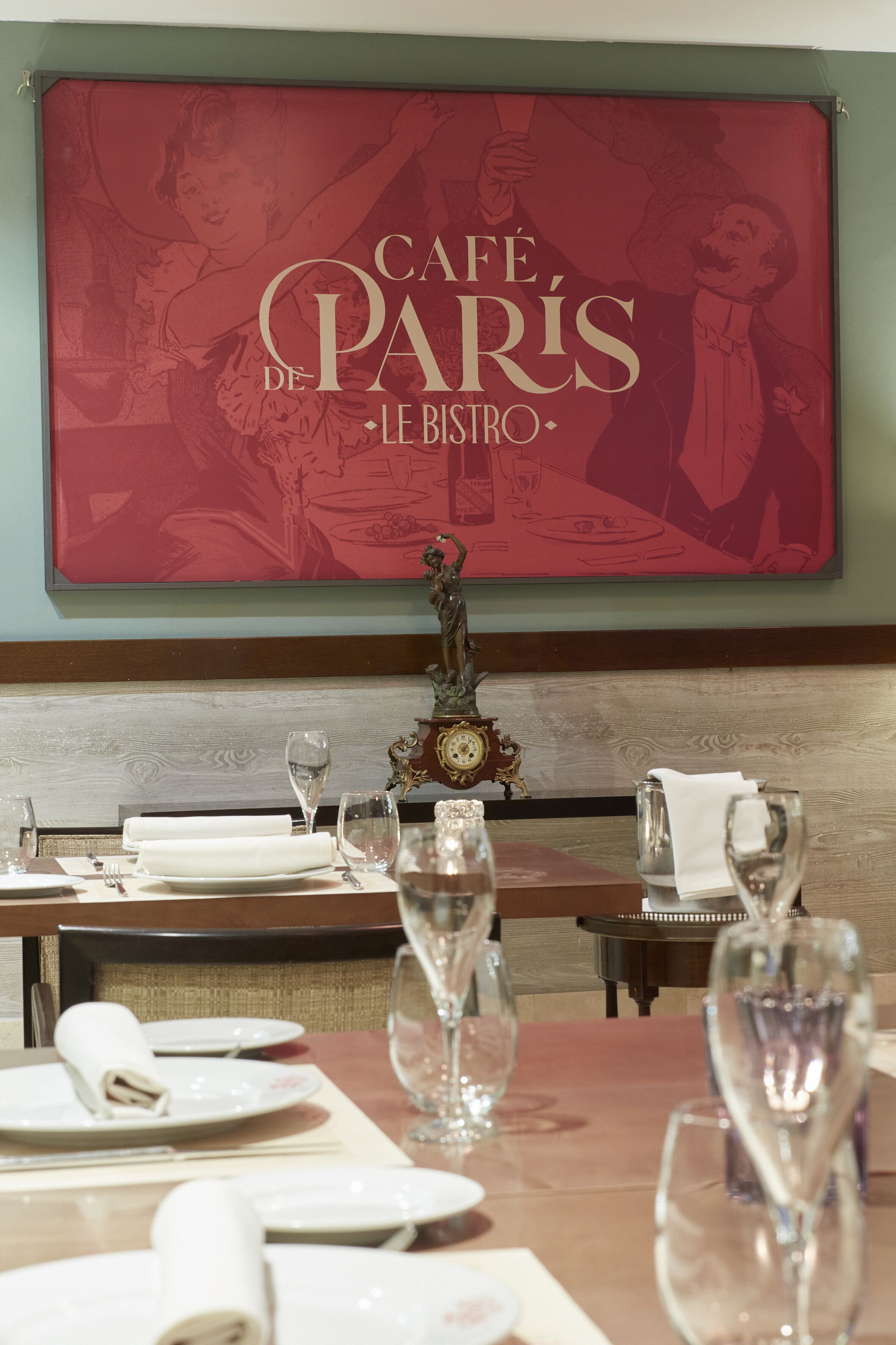 Una mesa de comedor dispuesta con platos, cubiertos y copas de vino, con un reloj decorativo y un menú enmarcado encima.