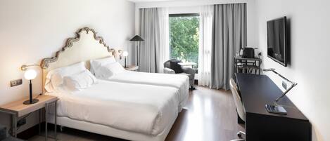 Habitación de hotel con dos camas, un escritorio, una silla, un televisor y una ventana con cortinas.