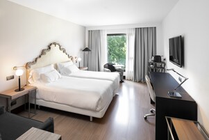 Quarto de hotel com duas camas, uma escrivaninha, uma cadeira, uma televisão e uma janela com cortinas.