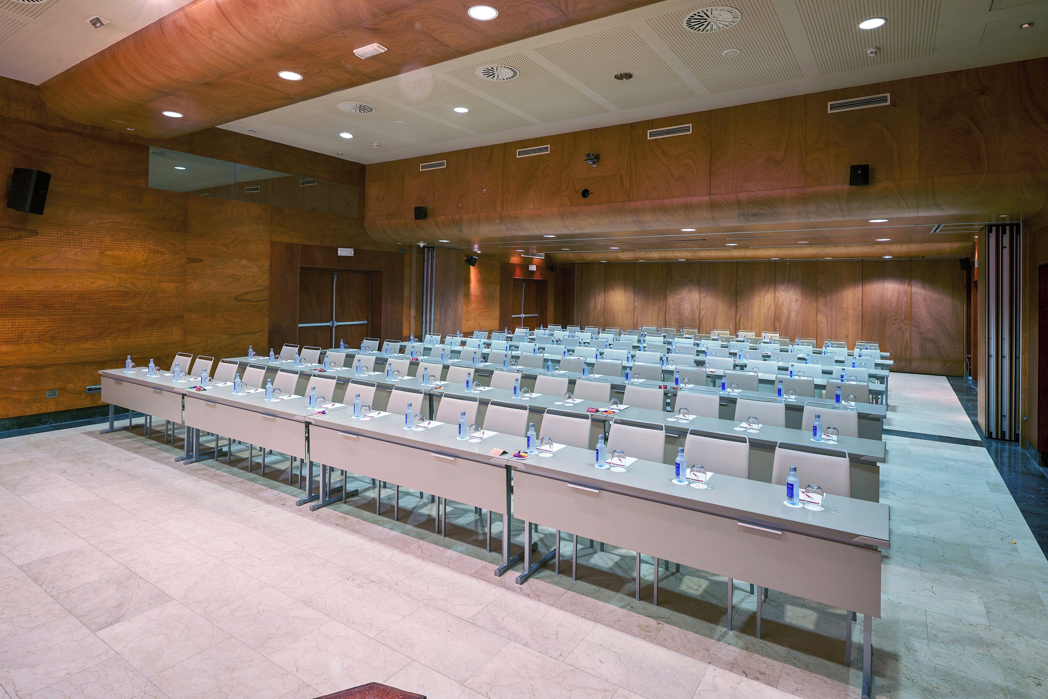 Un salón de conferencias con filas de mesas y sillas, equipado con tarjetas de identificación y botellas de agua.