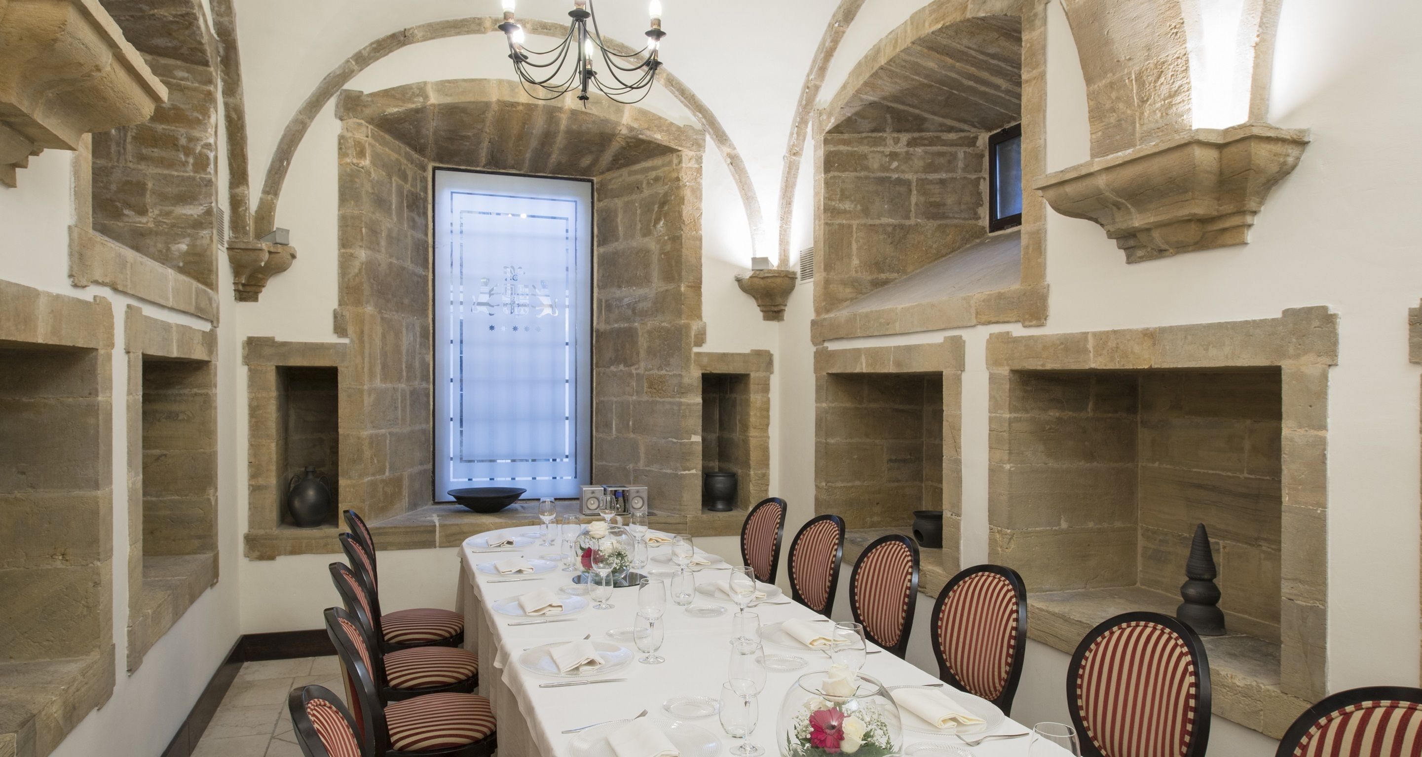 A dining room with a long table set for a meal, stone walls, and a large window.