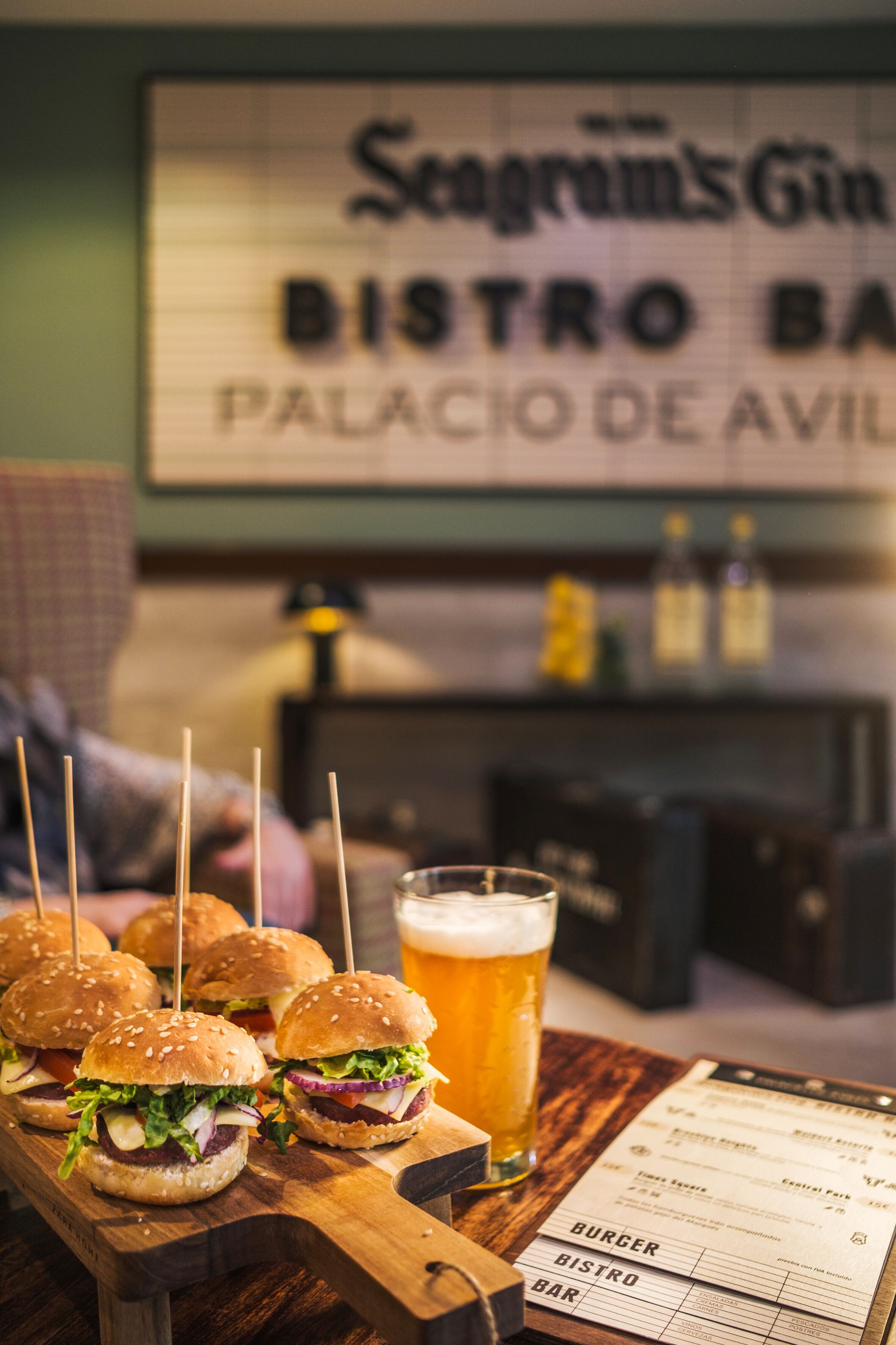 Una tabla de madera con mini hamburguesas y una jarra de cerveza, un menú y un letrero para Seagram's Gin Bistro Bar.