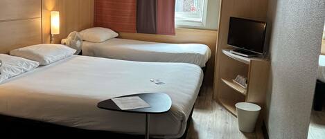 A hotel room with two beds, a TV, a small table with a menu, and a window with curtains.