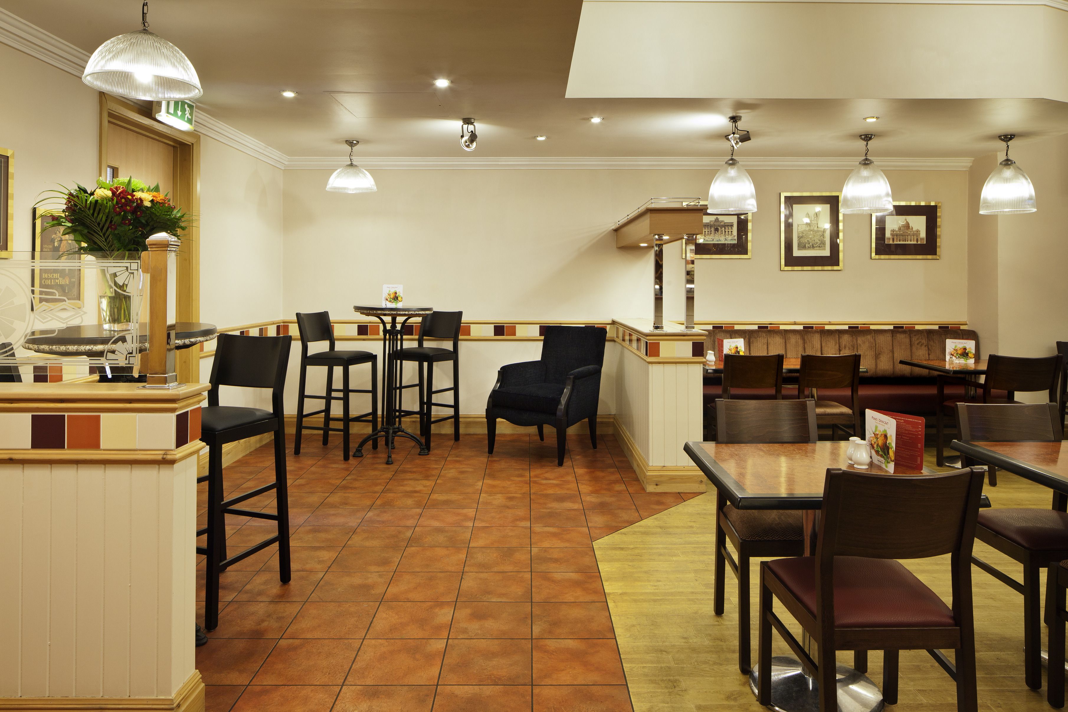 A restaurant with multiple tables and chairs, a counter with a cash register, and framed pictures on the wall.