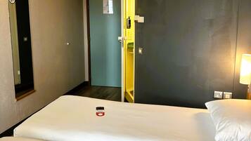 A hotel room with a bed, a nightstand with a lamp, a door, and a mirror.