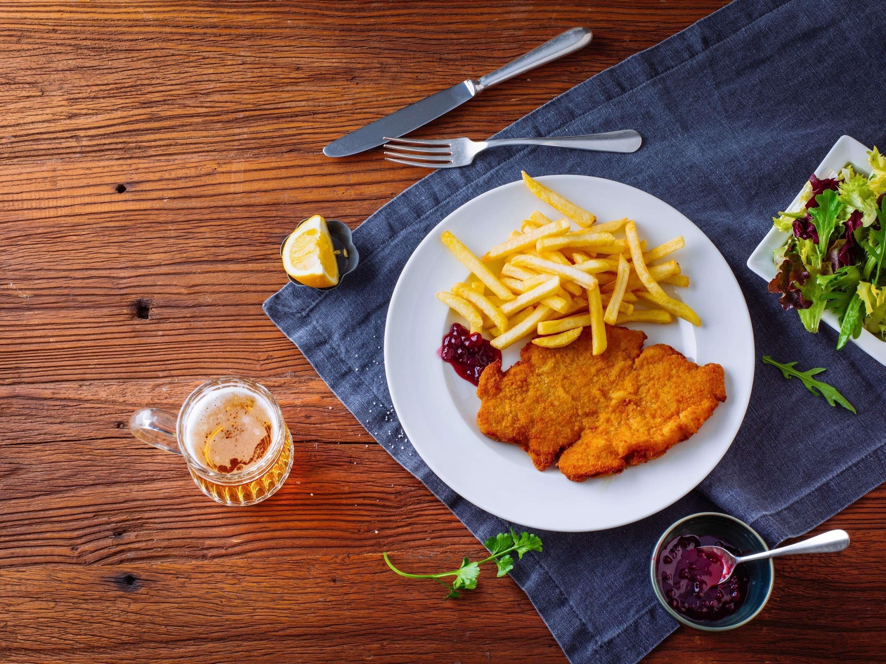 A plate of food with fries, a breaded cutlet, and a side salad on a wooden table.