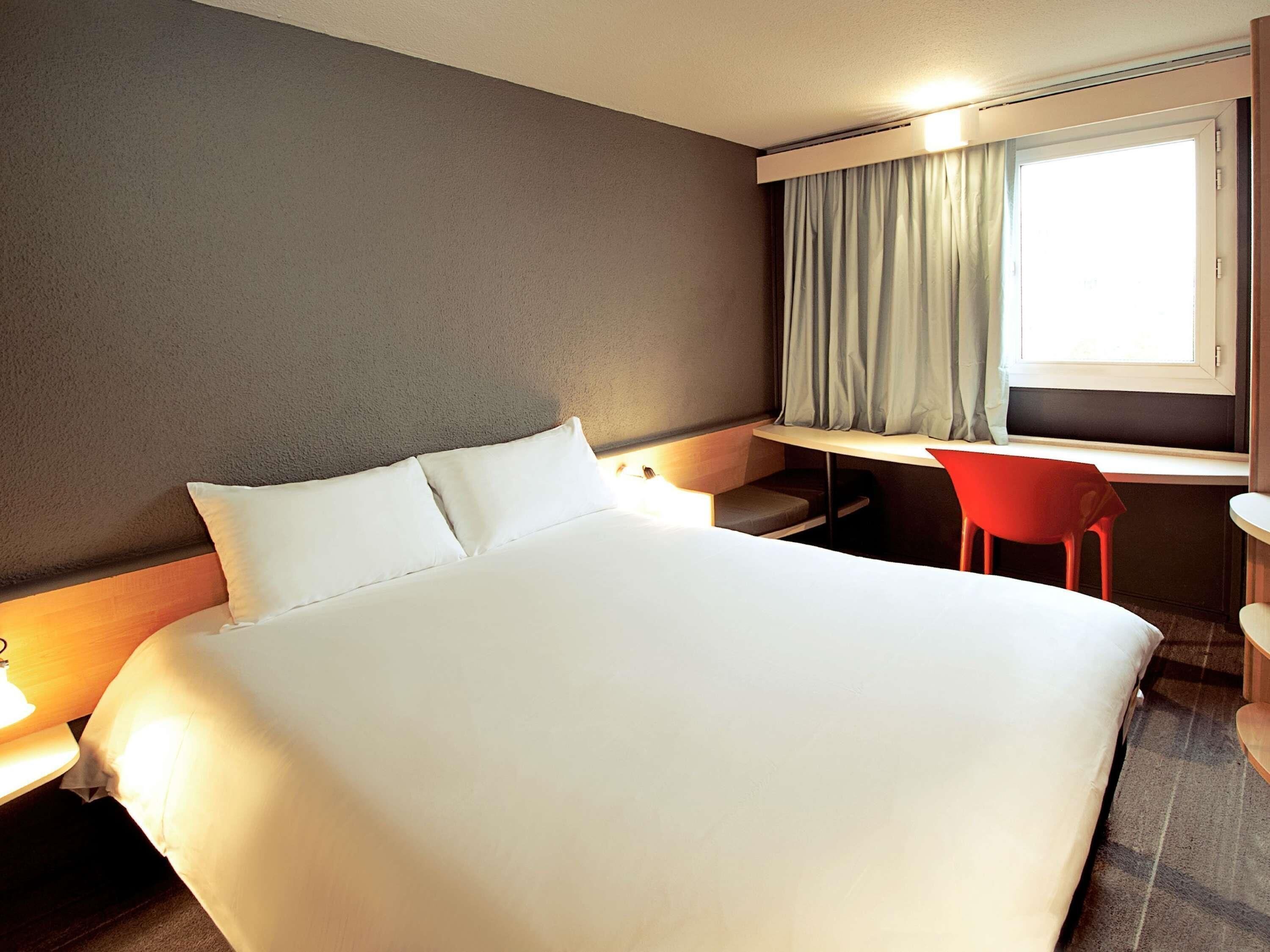 A hotel room with a bed, a desk, a chair, and a window with curtains.
