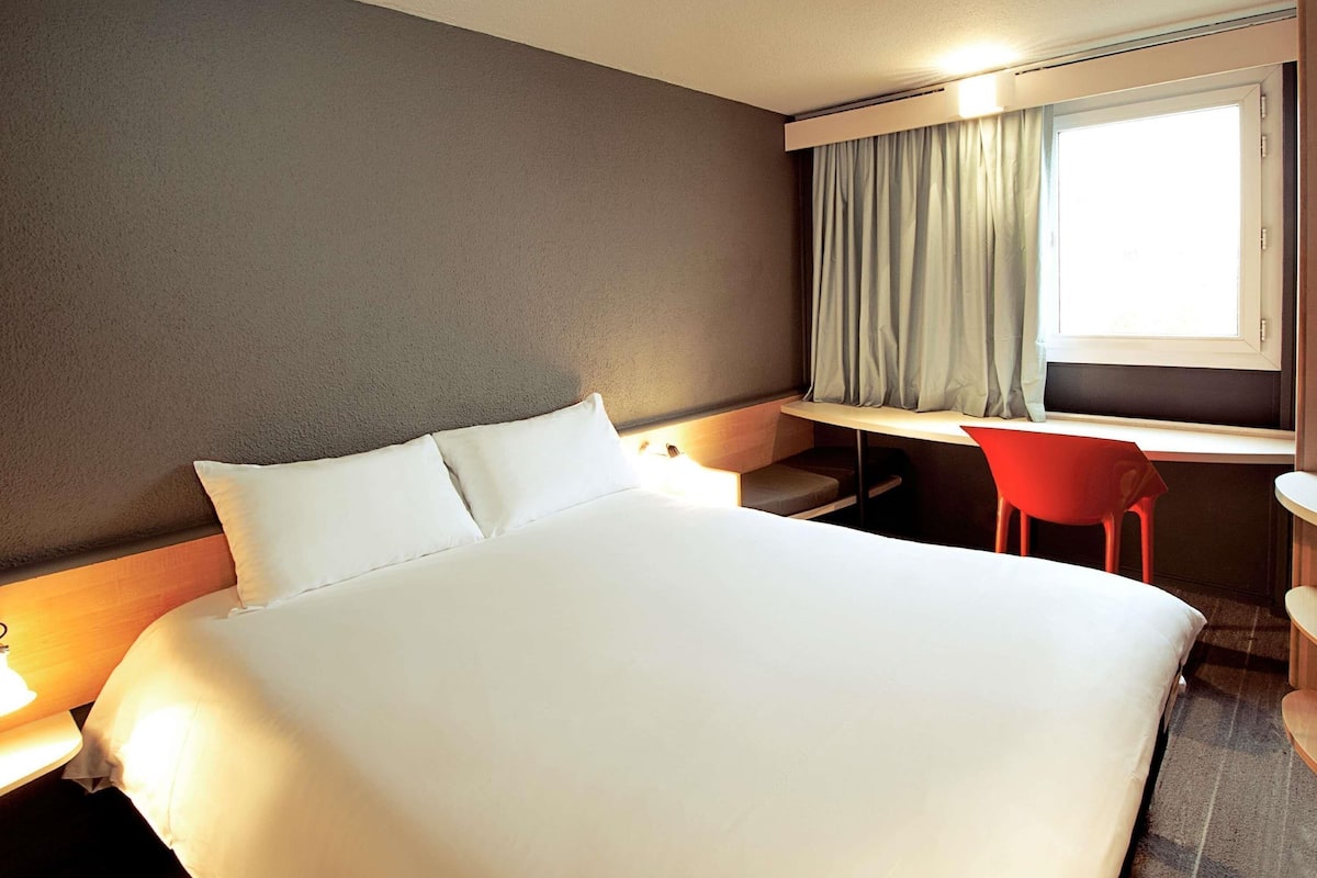 A hotel room with a bed, a desk, a chair, and a window with curtains.