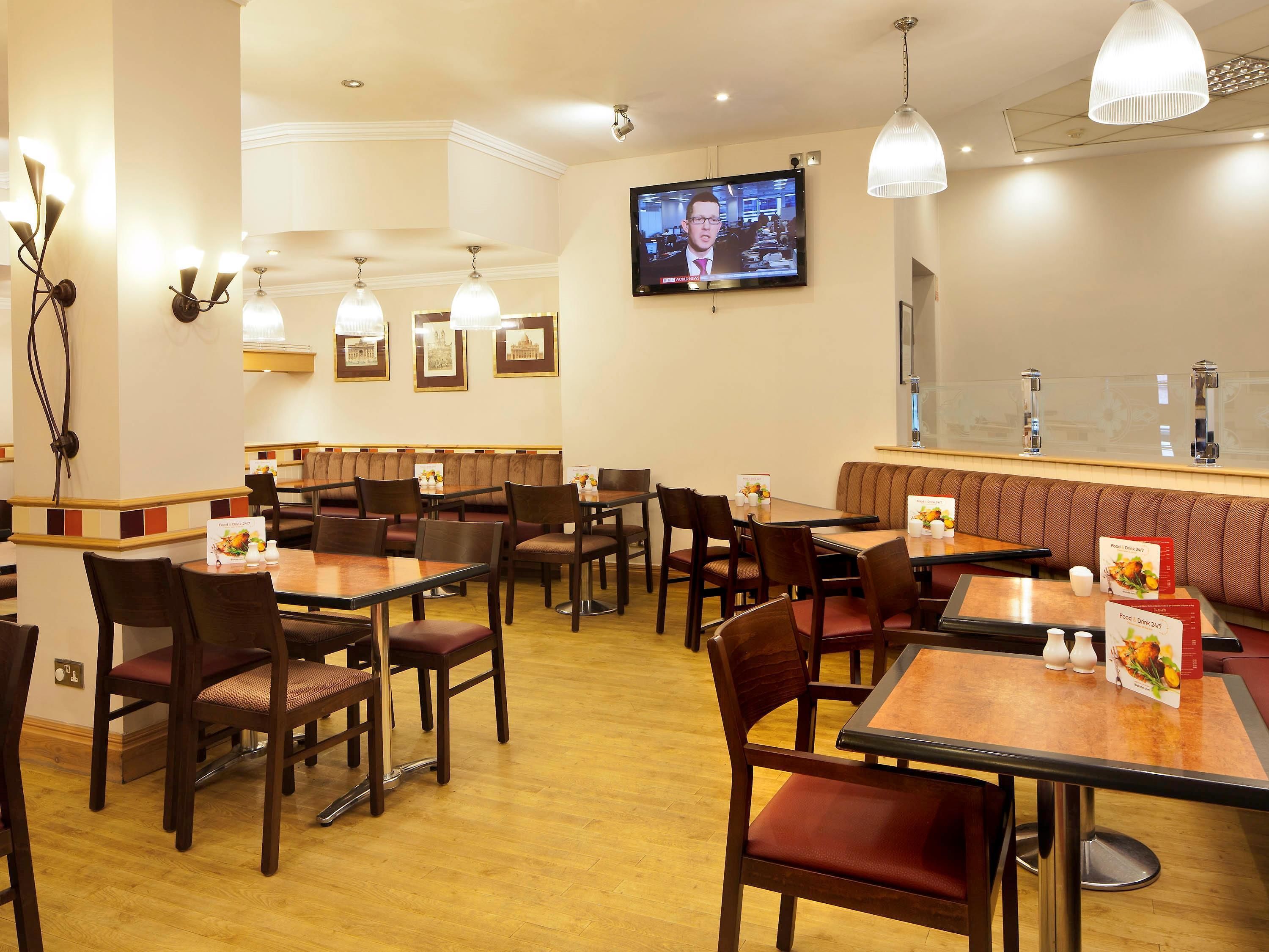 A restaurant with wooden tables and chairs, a television mounted on the wall, and a bar area with a high counter.