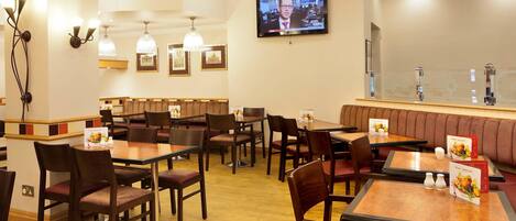 A restaurant with wooden tables and chairs, a television mounted on the wall, and a bar area with a high counter.
