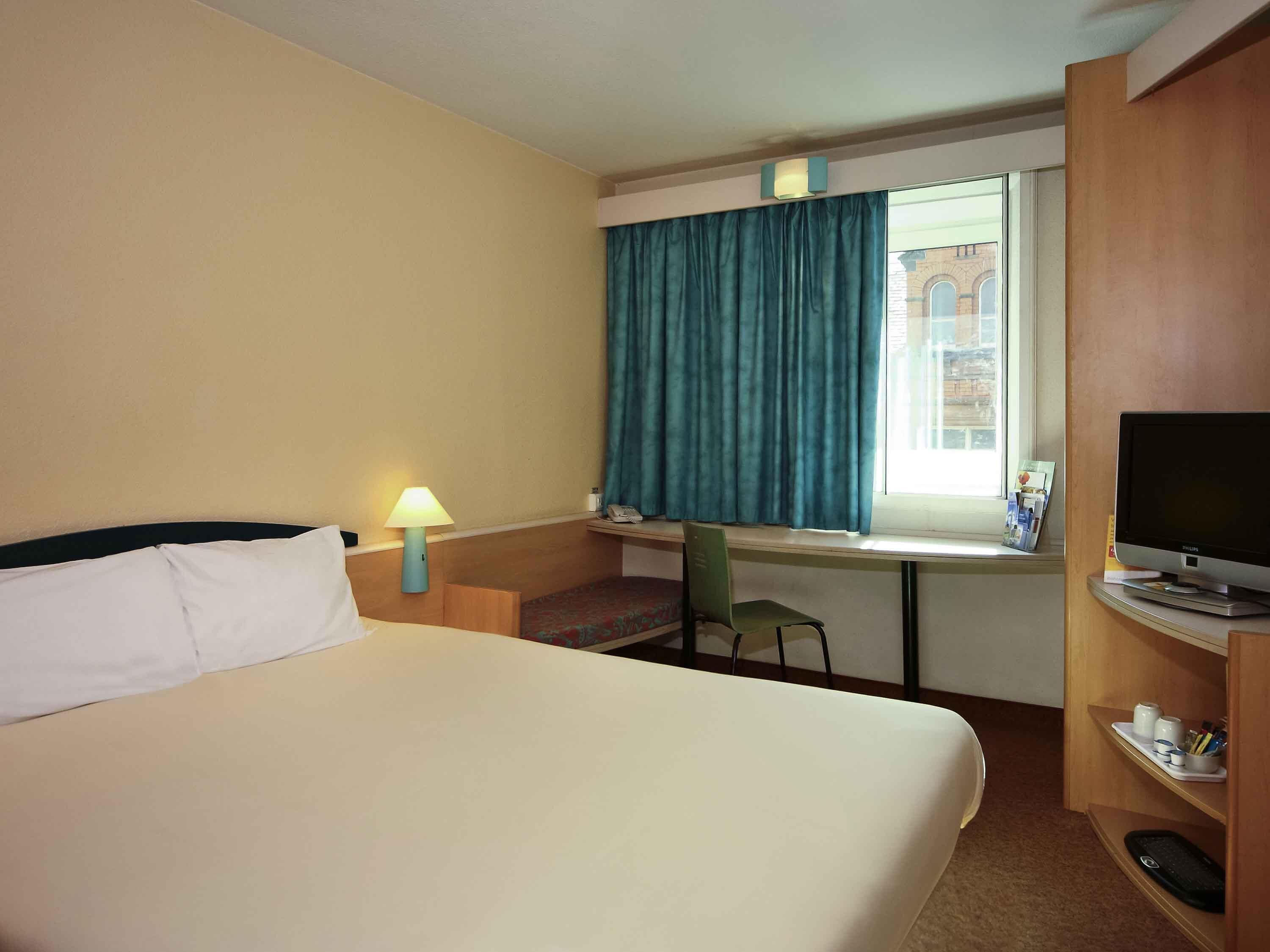 Une chambre d’hôtel équipée d’un lit, d’un bureau, d’une chaise, d’une télévision et d’une fenêtre avec des rideaux.