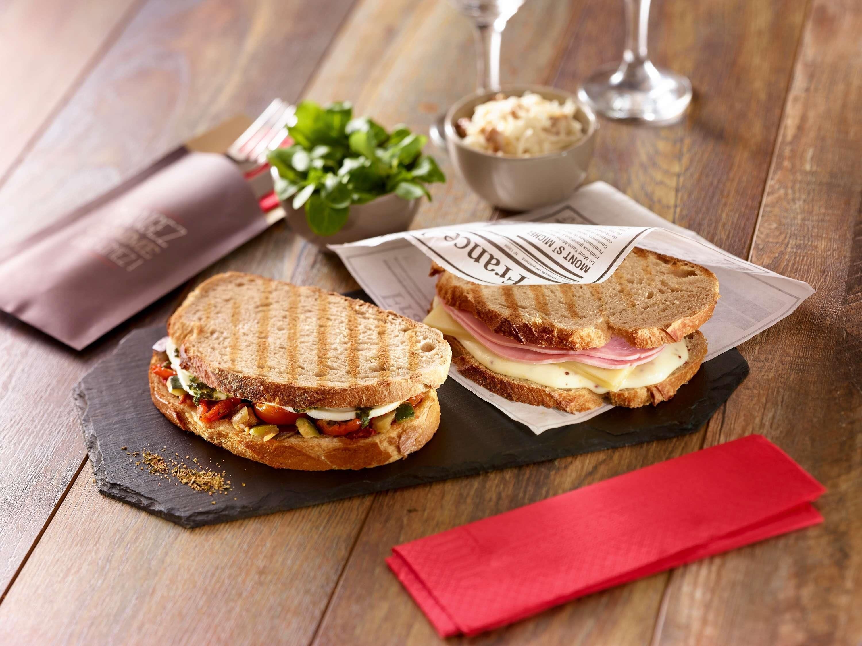 To sandwicher på en skiferplade med en rød serviet og et glas vand.