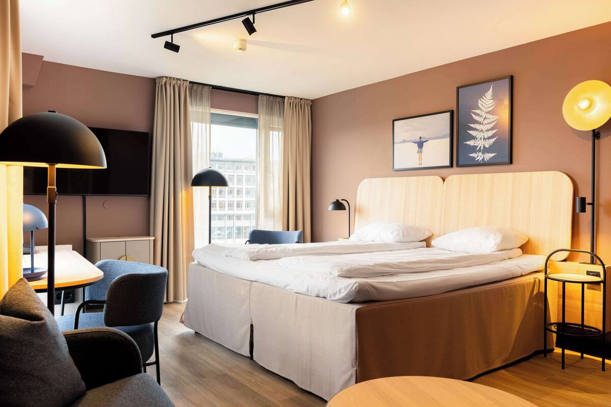 A modern hotel room with a bed, a desk, a chair, and a TV.