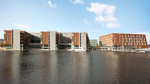 A modern building complex with multiple floors, a waterfront view, and a marina with boats. - Scandic Nidelven (Trondheim)