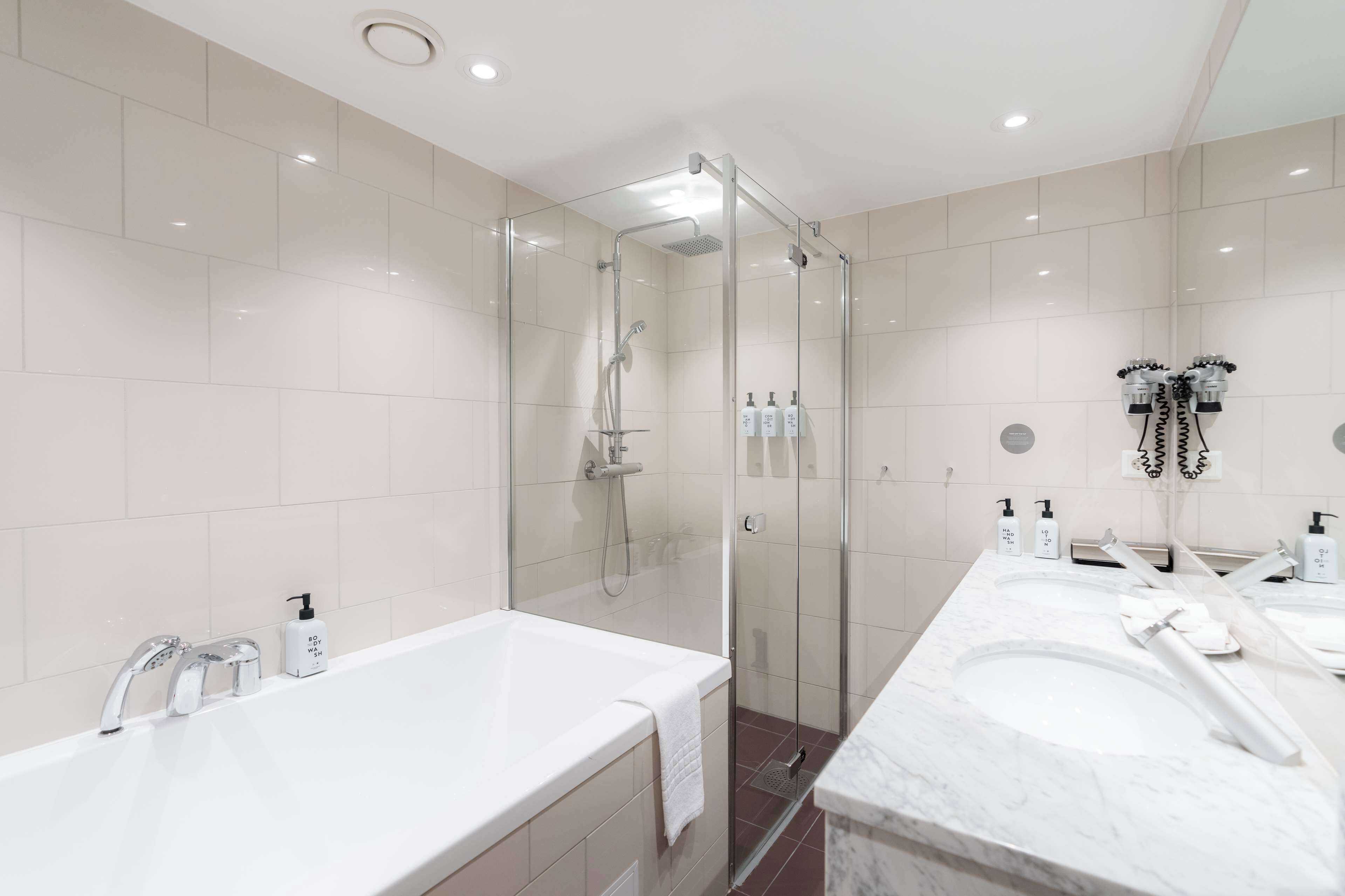 Un baño moderno con ducha de mampara de vidrio, dos lavamanos y una bañera grande.