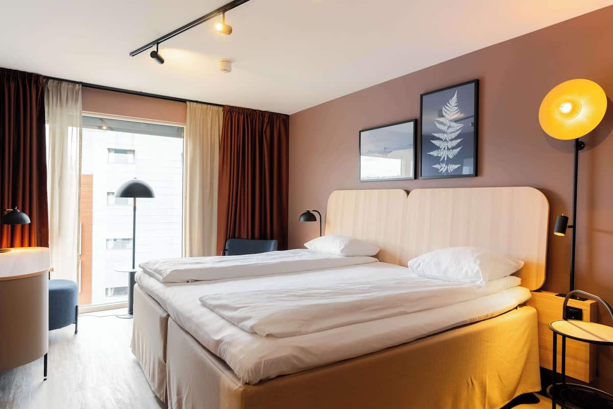 A hotel room with two beds, a desk, a chair, and a window with curtains.