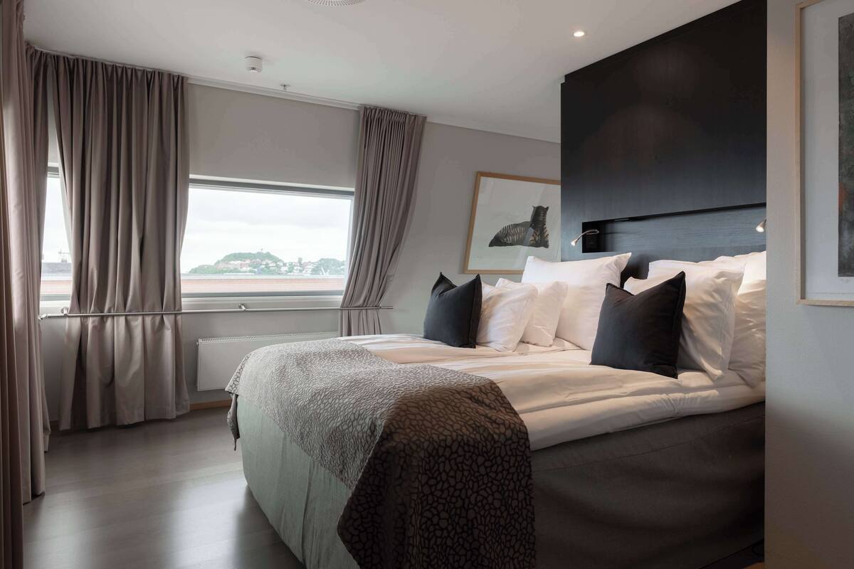 A modern bedroom with a large bed, a headboard, and a window with curtains.
