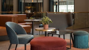 A modern lounge area with seating arrangements, a round table with a plant, and a view through large windows. - Scandic Nidelven (Trondheim)