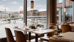 A dining area with tables set for two, overlooking a marina with boats and buildings in the background. - Scandic Nidelven (Trondheim)