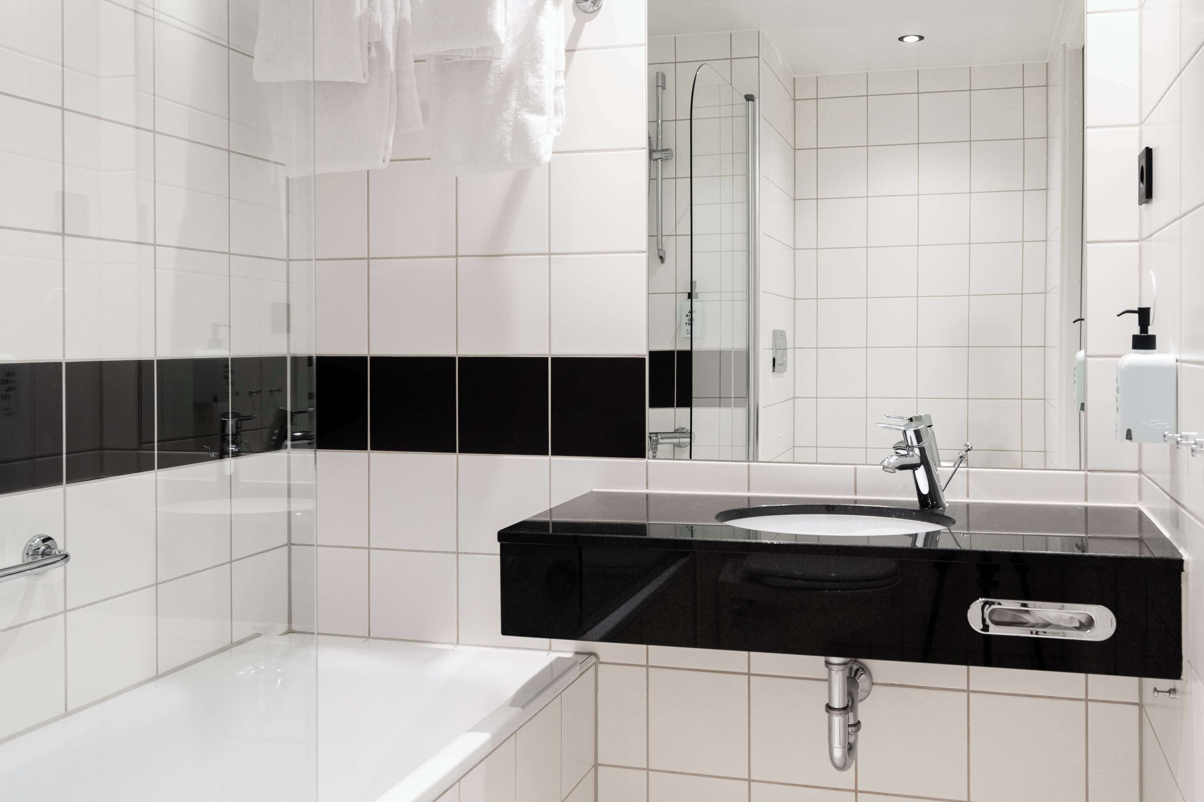 A modern bathroom with white tiles, a black countertop, a white sink, and a glass-enclosed shower.
