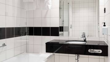 A modern bathroom with white tiles, a black countertop, a white sink, and a glass-enclosed shower.