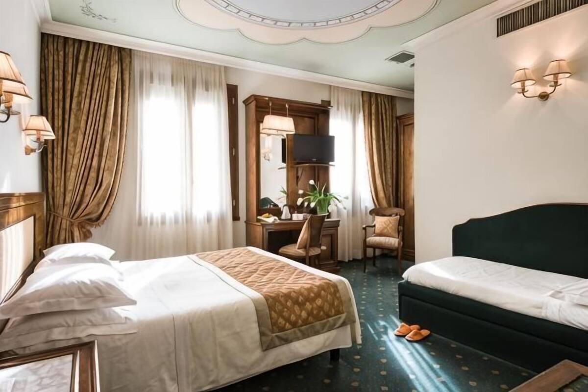 A hotel room with two beds, a desk, a chair, a TV, and a window with curtains.