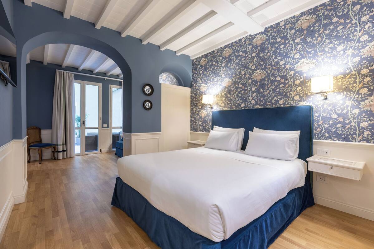 A bedroom with a large bed, a nightstand, a wall-mounted lamp, and a view through an archway to another room.