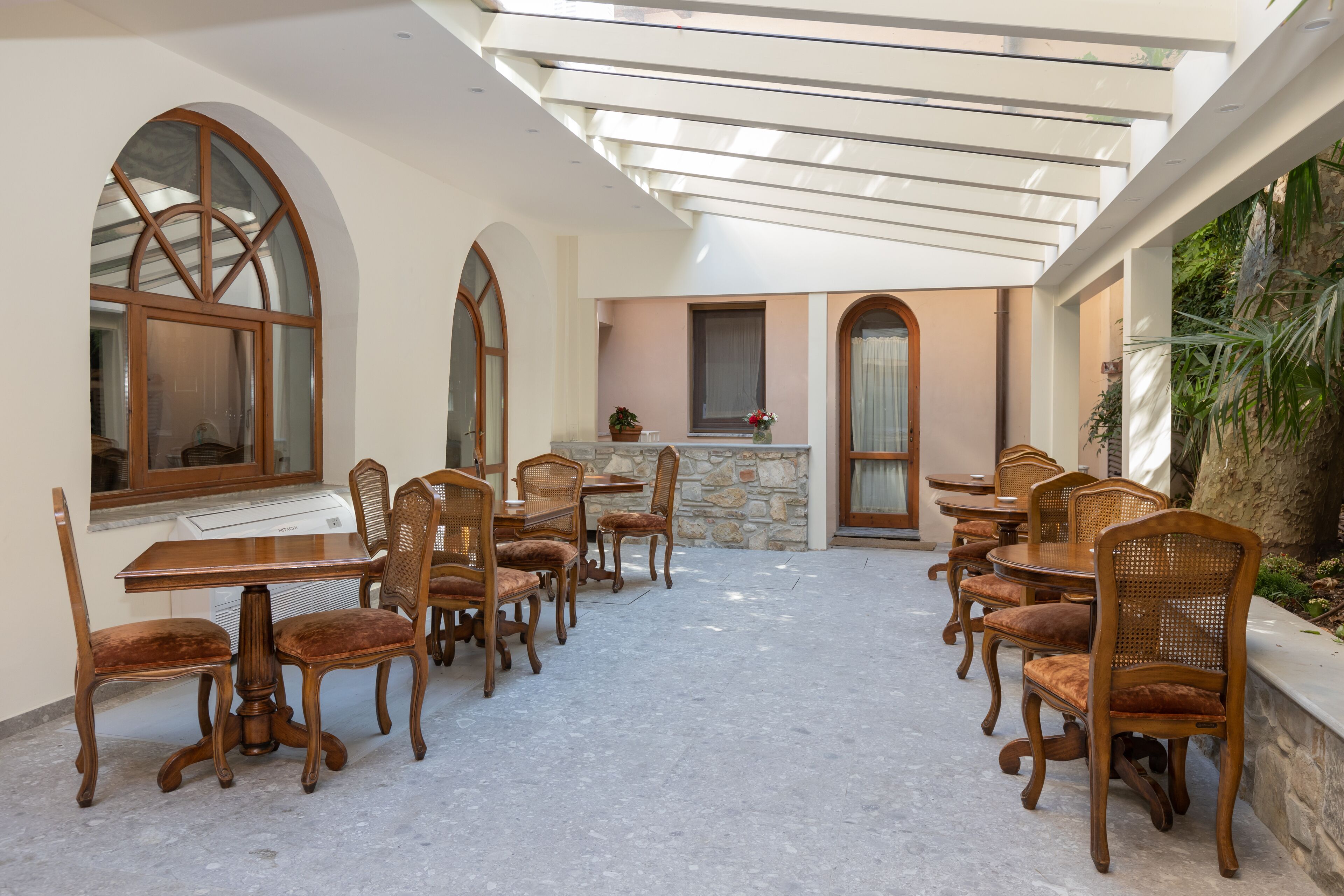 Un portico coperto con un muro in pietra, tavoli e sedie in legno e un piccolo angolo cottura.
