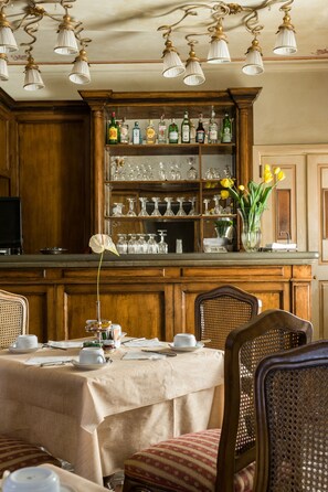 Un coin repas avec un bar en bois, une table dressée pour quatre personnes et une variété de verres exposés sur des étagères.