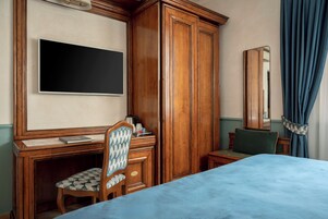 Habitación de hotel con cama, escritorio con silla, armario, televisor de pantalla plana y espejo.