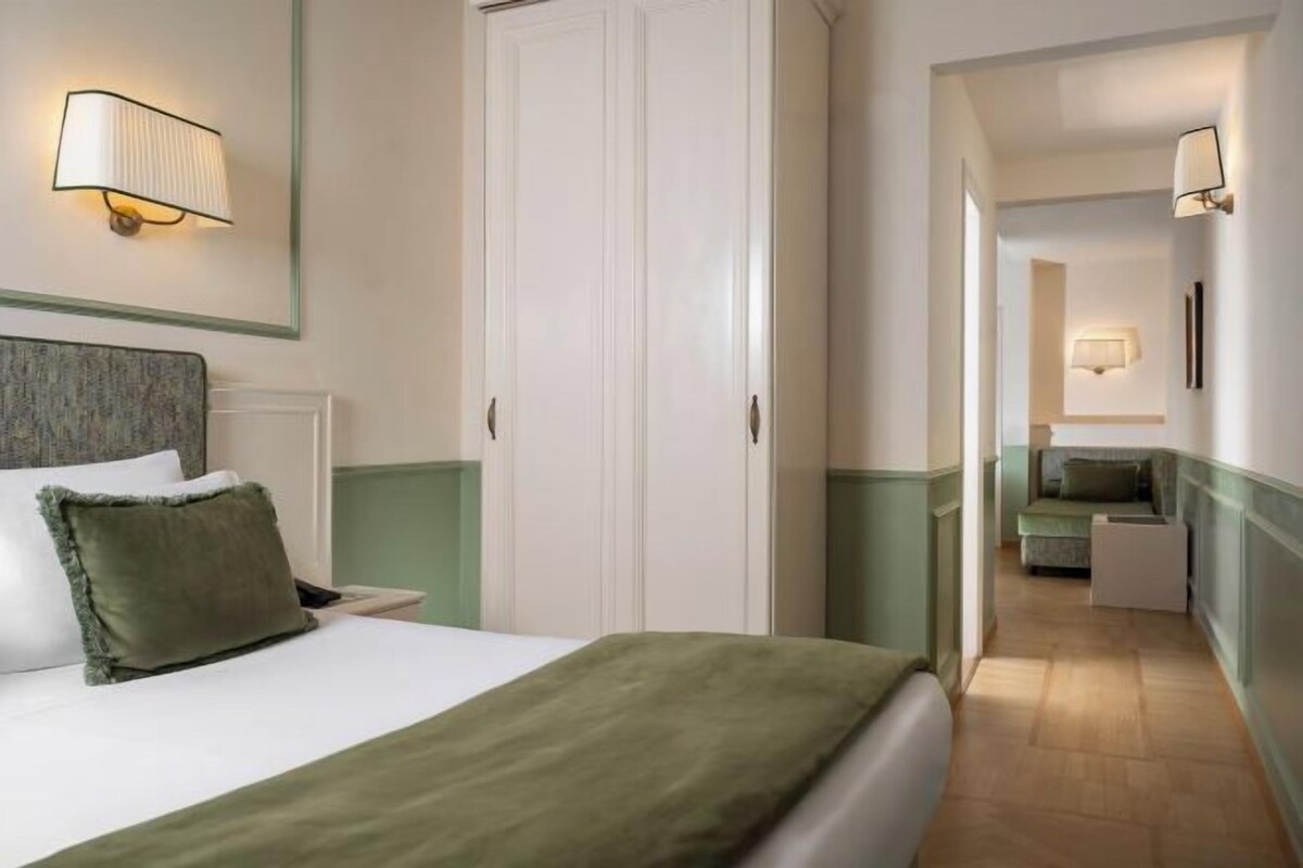Una camera d'albergo con un letto, un comodino e una coperta verde.