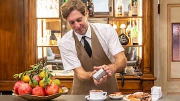 A bar setting with a bartender preparing a drink, a fruit bowl, and a coffee cup on the counter.
