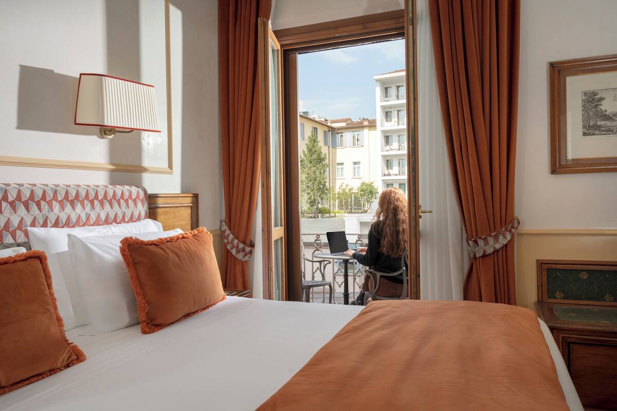 A hotel room with a bed, a desk, and a view of the outside.
