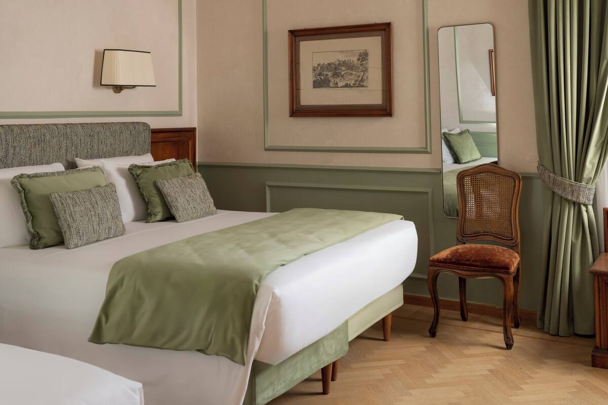 A hotel room with a large bed, a chair, a mirror, and a picture on the wall.