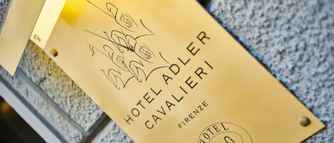 Ein goldfarbenes Hotelschild mit dem Schriftzug "HOTEL ADLER CAVALIERI" und dem Ortsnamen "FIRENZE".
