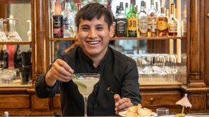 A person seated at a bar with a drink in front of them, a plate of snacks, and a bar stocked with various bottles. - Hotel Adler Cavalieri (Florence)