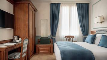 Una habitación de hotel con cama, escritorio, silla, armario, espejo y ventana con cortinas.