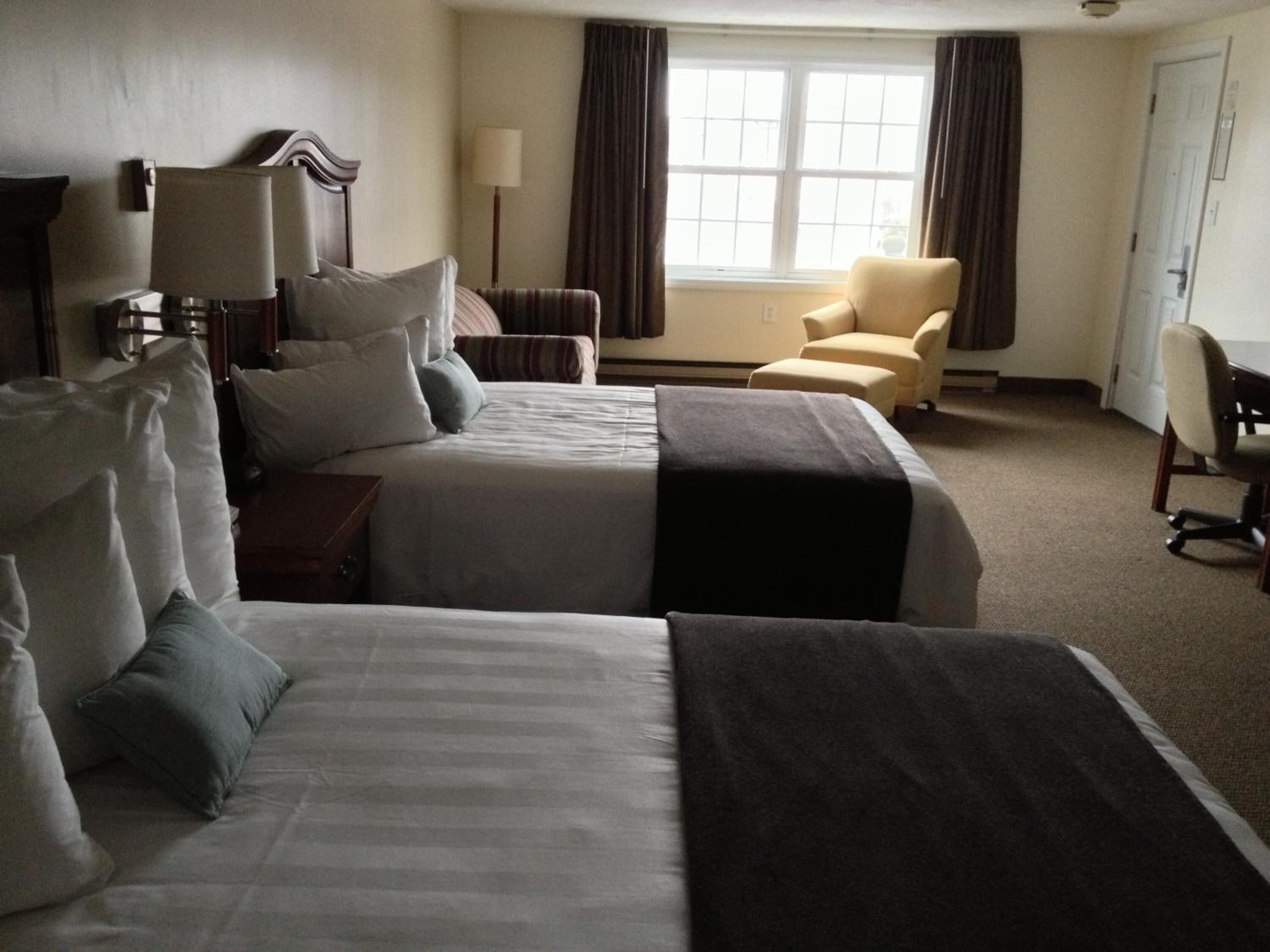 Ein Hotelzimmer mit zwei Betten, einem Schreibtisch, einem Stuhl und einem Vorhangfenster.