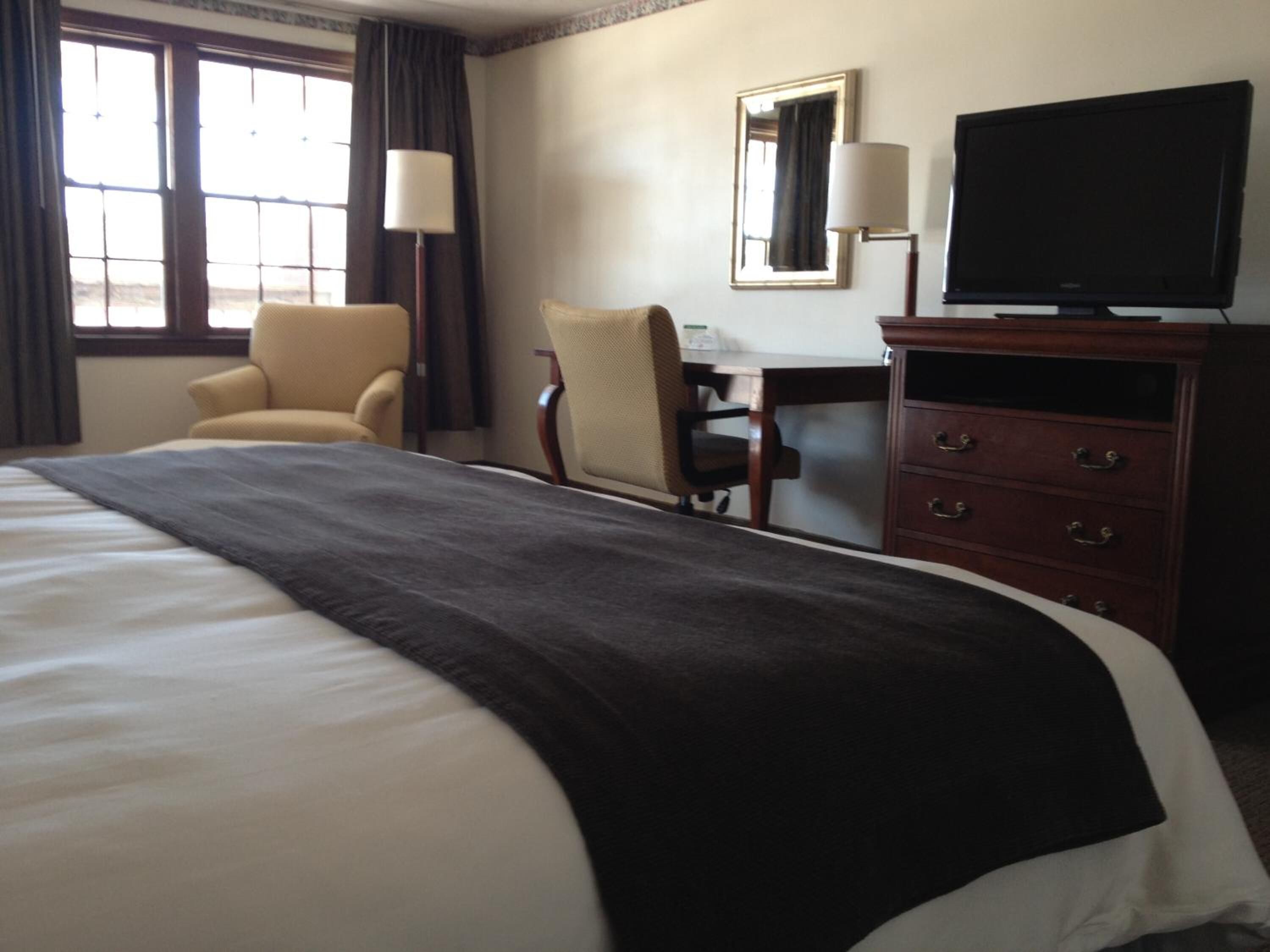 A hotel room with a large bed, a desk, a chair, a television, and a dresser.