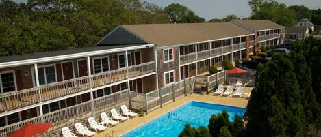 A hotel with a pool area, multiple balconies, and a fenced deck with lounge chairs.