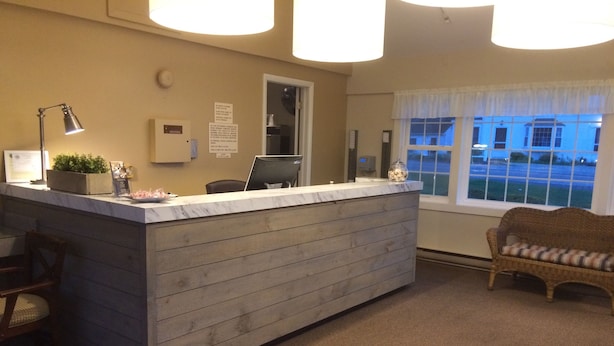 A reception desk with a marble top, a wooden panel base, a desk lamp, a potted plant, and a wicker chair with a cushion.