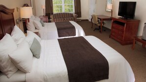 A hotel room with two beds, a desk, a television, and a window with curtains.