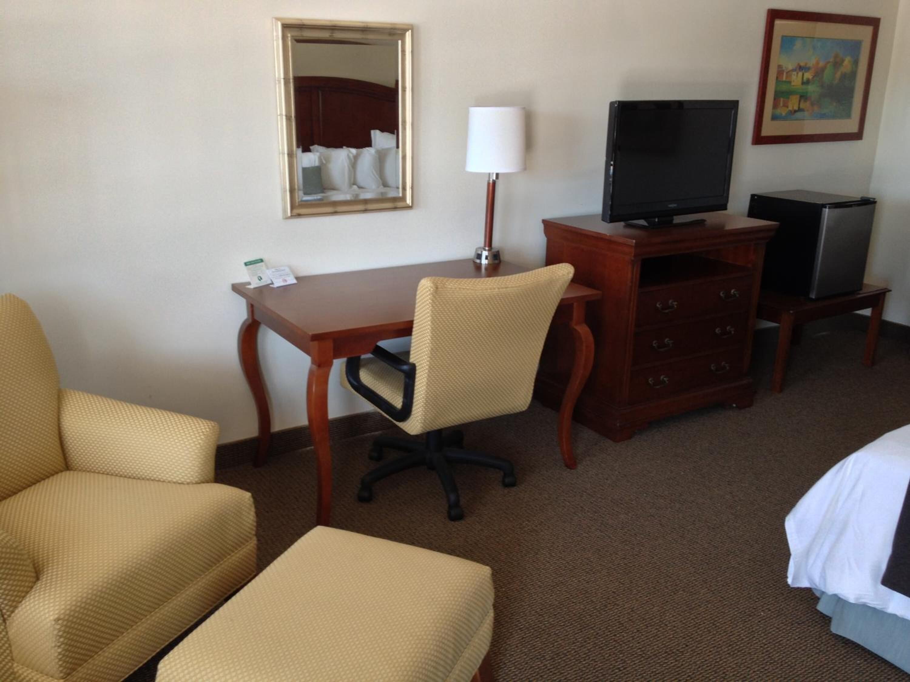 A hotel room with a bed, a desk with a chair, a television, a dresser, and a mirror.