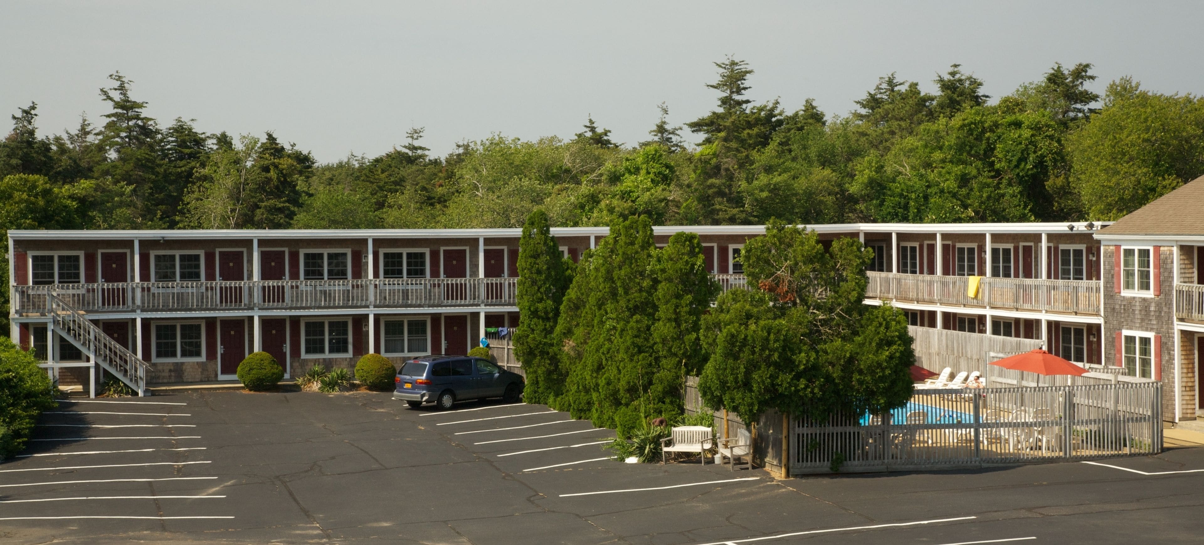 A motel with a two-story structure, a parking lot, and a fenced pool area.