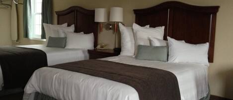 A hotel room with two beds, a nightstand with a lamp, and a window with curtains.