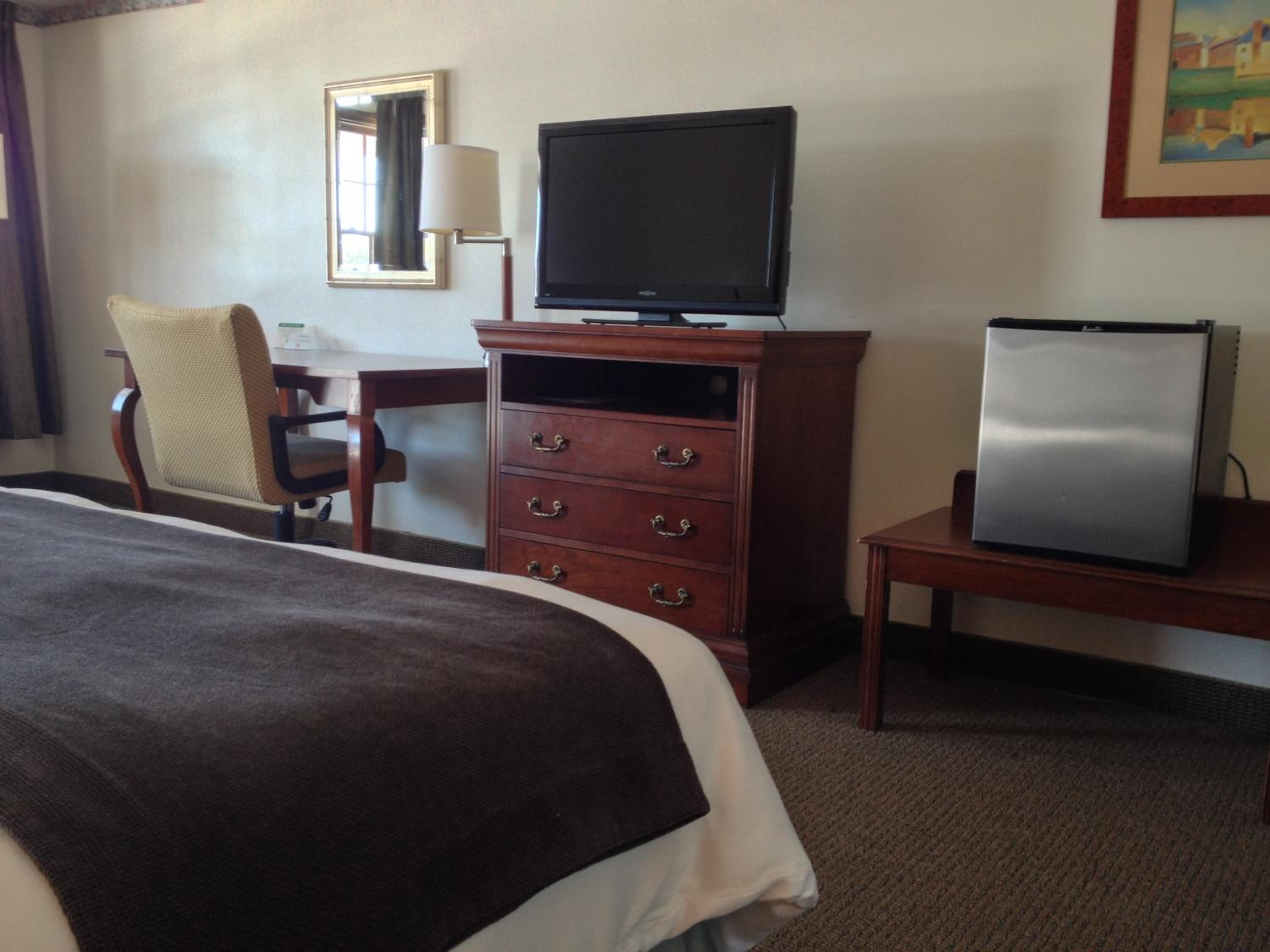 A hotel room with a bed, a wooden dresser, a television, and a refrigerator.