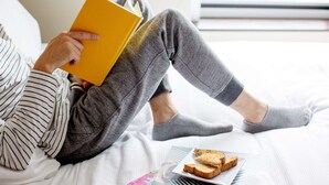 Une personne assise sur un lit, un livre à la main et deux tranches de pain grillé à côté d’elle.