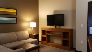 Une chambre d’hôtel avec un canapé, un téléviseur posé sur un meuble en bois, une lampe et deux tableaux encadrés accrochés au mur.