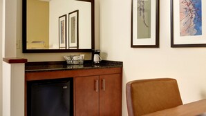 Une chambre d’hôtel avec un meuble en bois, un réfrigérateur, une machine à café et un tableau encadré au mur.