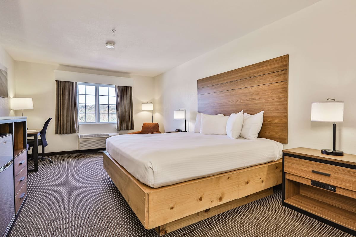 A hotel room with a large bed, a desk, a chair, and a nightstand.